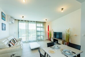 Una sala moderna con sofá, mesa de comedor, televisor y plantas en macetas.