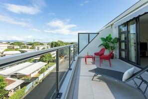 A balcony with a glass railing, a red chair, a lounge chair, and a potted plant. - Atea Pearl (Pirae)