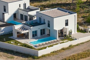 A modern two-story house with a swimming pool, outdoor seating, and a landscaped garden.