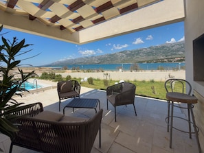 A terrace with wicker furniture, a pool, and a view of the sea and mountains.