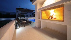 Un patio exterior con piscina, sillones de descanso y chimenea.