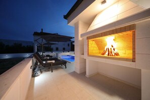 An outdoor patio with a pool, lounge chairs, and a fireplace. - Villa Mariva with Heated Pool (Vir)