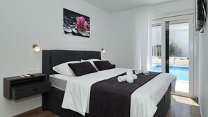 Habitación de hotel moderna con una cama, una mesita de noche, un cuadro y vista a una piscina al aire libre.