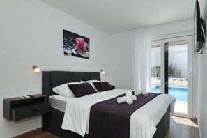 A modern hotel room with a bed, a nightstand, a painting, and a view of an outdoor swimming pool. - Villa Mariva with Heated Pool (Vir)