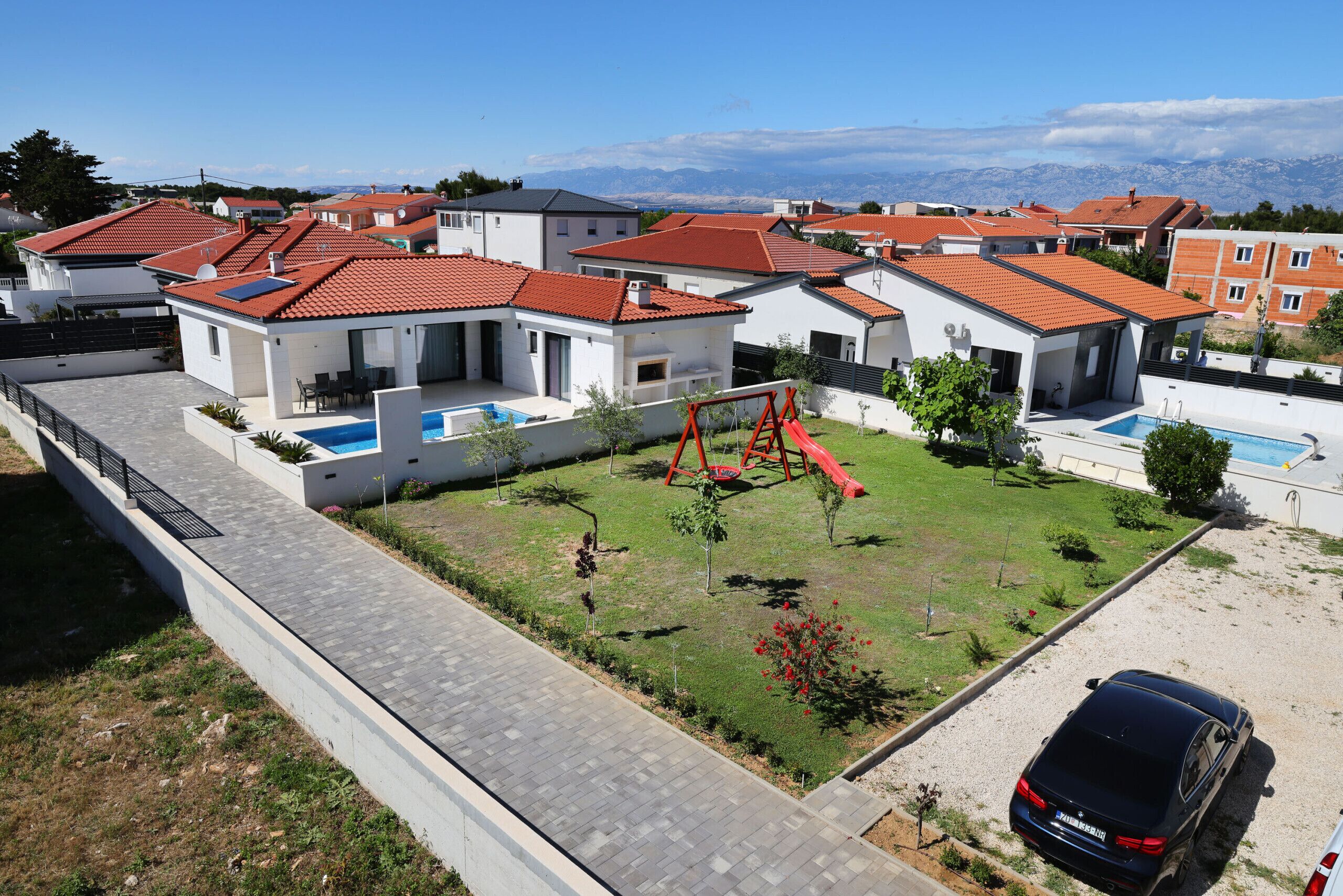 A residential area with modern houses, a swimming pool, and a red swing set.