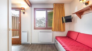 Una habitació amb un llit, un televisor penjat a la paret, una finestra amb vista a muntanyes nevades i un radiador.