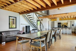 A spacious living area with a wooden dining table, a sofa, and a staircase leading to an upper level.