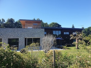 Un bâtiment moderne à deux étages, doté d’une façade en pierre et de grandes fenêtres, entouré d’un jardin bien entretenu.