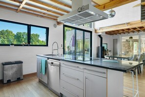 A modern kitchen with a large island, a dishwasher, and a view of the outdoors. - Villa "Samagestia" with Indoor Pool and Jacuzzi (Saint-Médard-sur-Ille)