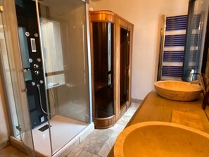 A bathroom with a glass-enclosed shower, a wooden bathtub, and a large basin.