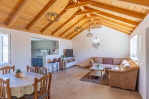 A spacious living area with a wooden ceiling, a dining table with chairs, a sofa, and a kitchen area with a TV. - Holiday Home Fortica with Sea View (Ražanac)