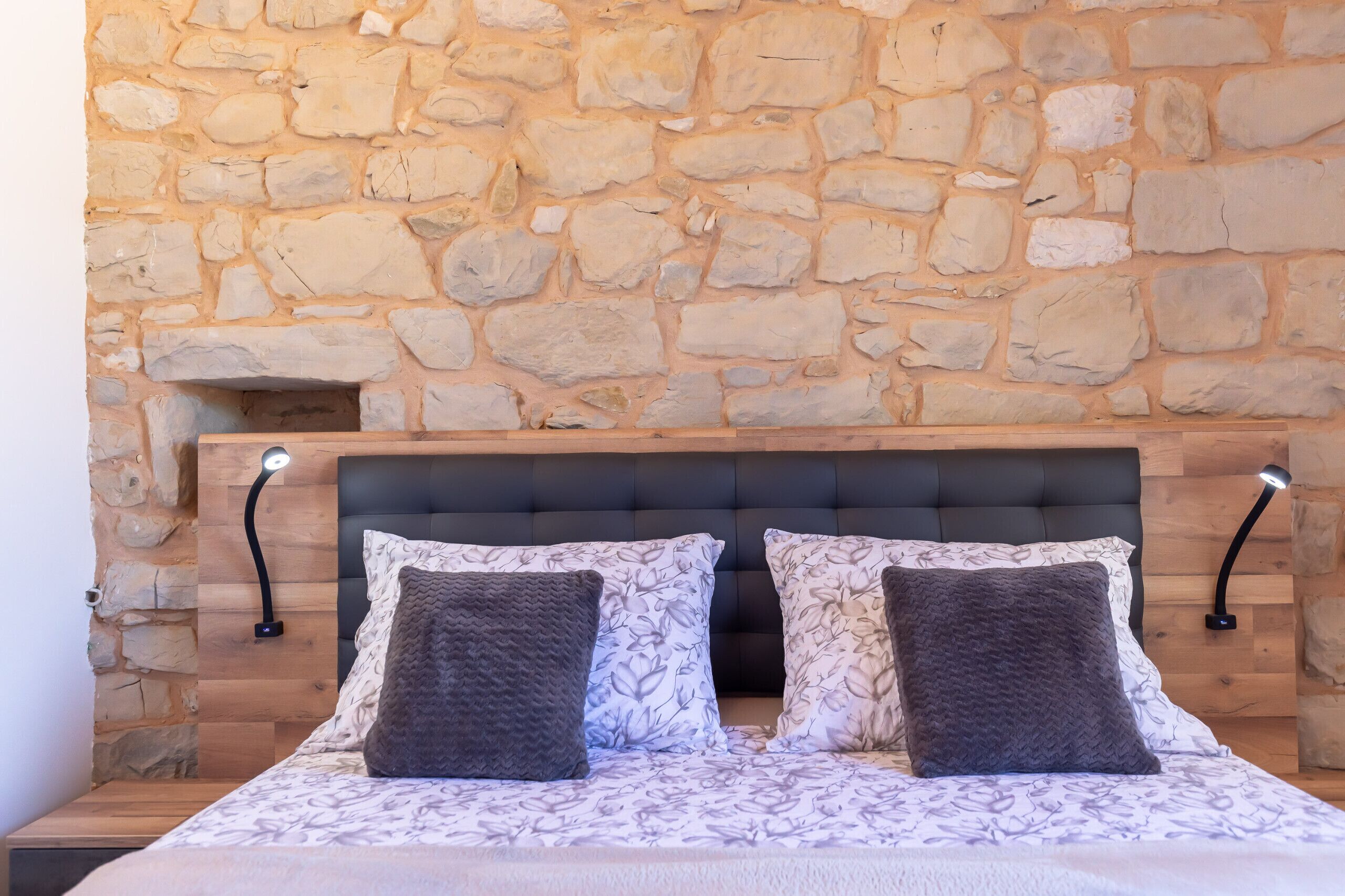 A bedroom with a stone wall, a bed with patterned bedding, and two bedside lamps.