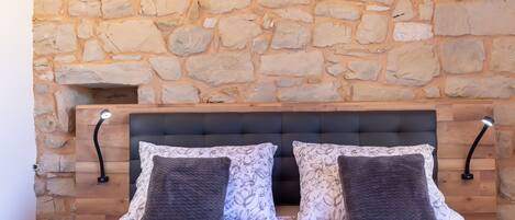 A bedroom with a stone wall, a bed with patterned bedding, and two bedside lamps.