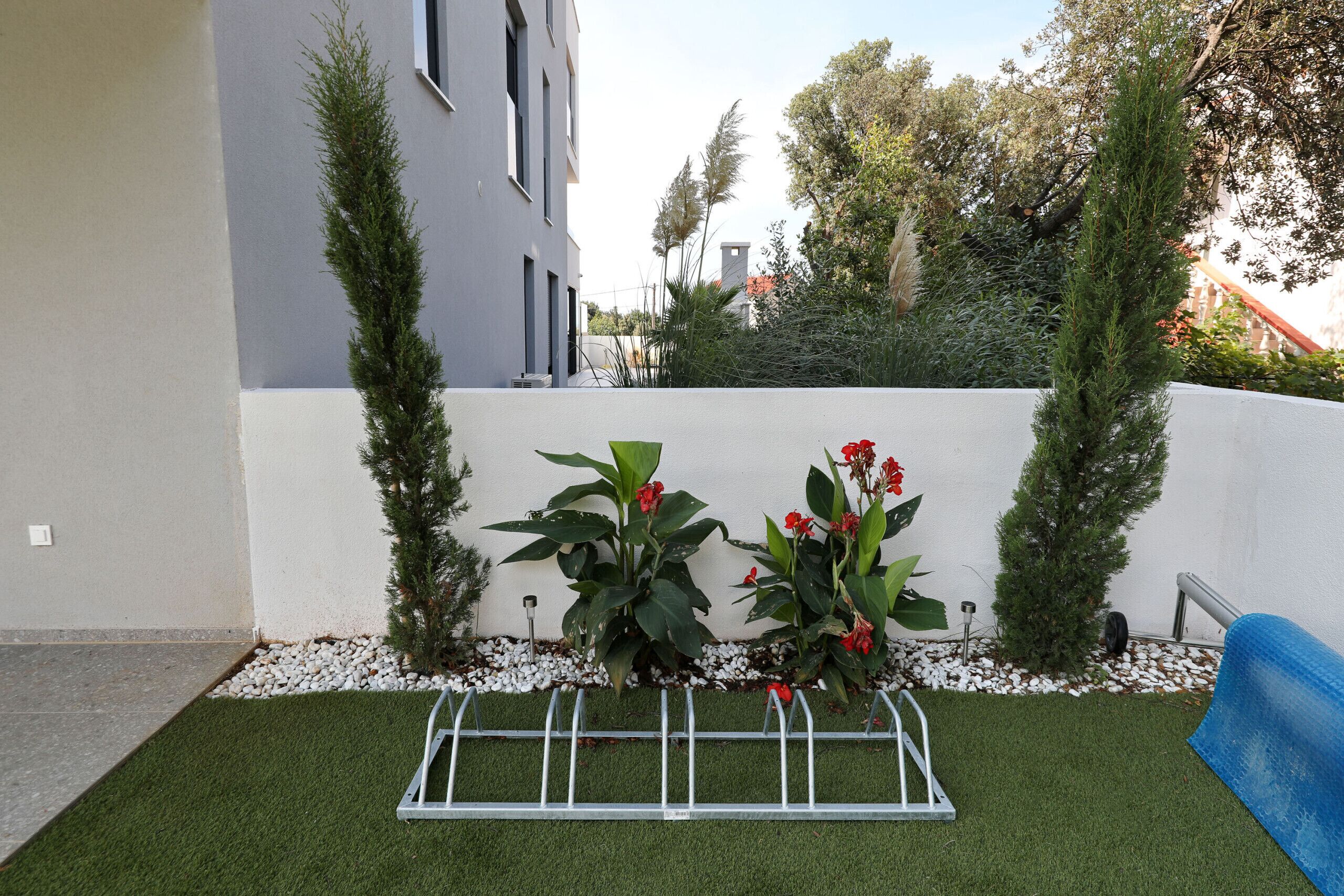 A modern building with a white facade, a small garden with artificial grass, and a metal structure in the foreground.