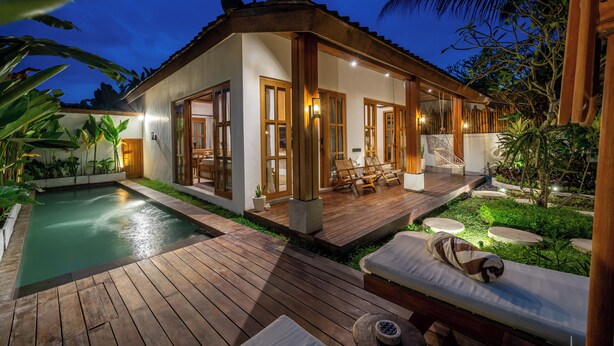 Een modern huis met een zwembad, houten terras en een loungehoek.
