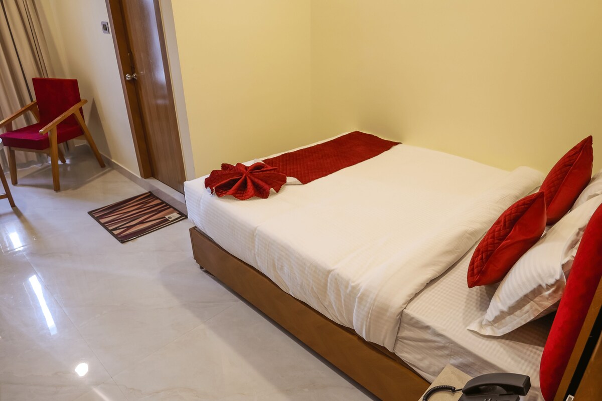 Una habitación de hotel con una cama, una silla roja, una puerta de madera y un teléfono en la mesita de noche.