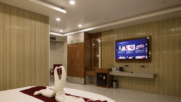 Een moderne hotelkamer met een groot bed, een flatscreen televisie aan de muur, een houten garderobe en een klein plankje met toiletartikelen.
