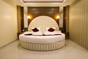 A round bed with a tufted headboard, two wall-mounted lights, and a mirror above. - Briddhishree Palace (Guwahati)