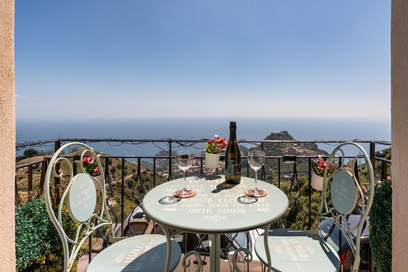 Eine Terrasse mit Tisch für Zwei, einer Weinflasche und Blick aufs Meer.