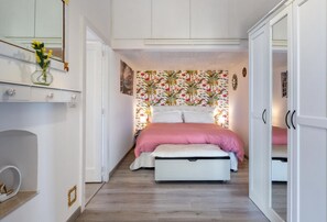 Ein Schlafzimmer mit einem Bett, einer Bank, einer Kommode und einer Wand mit floralem Muster.