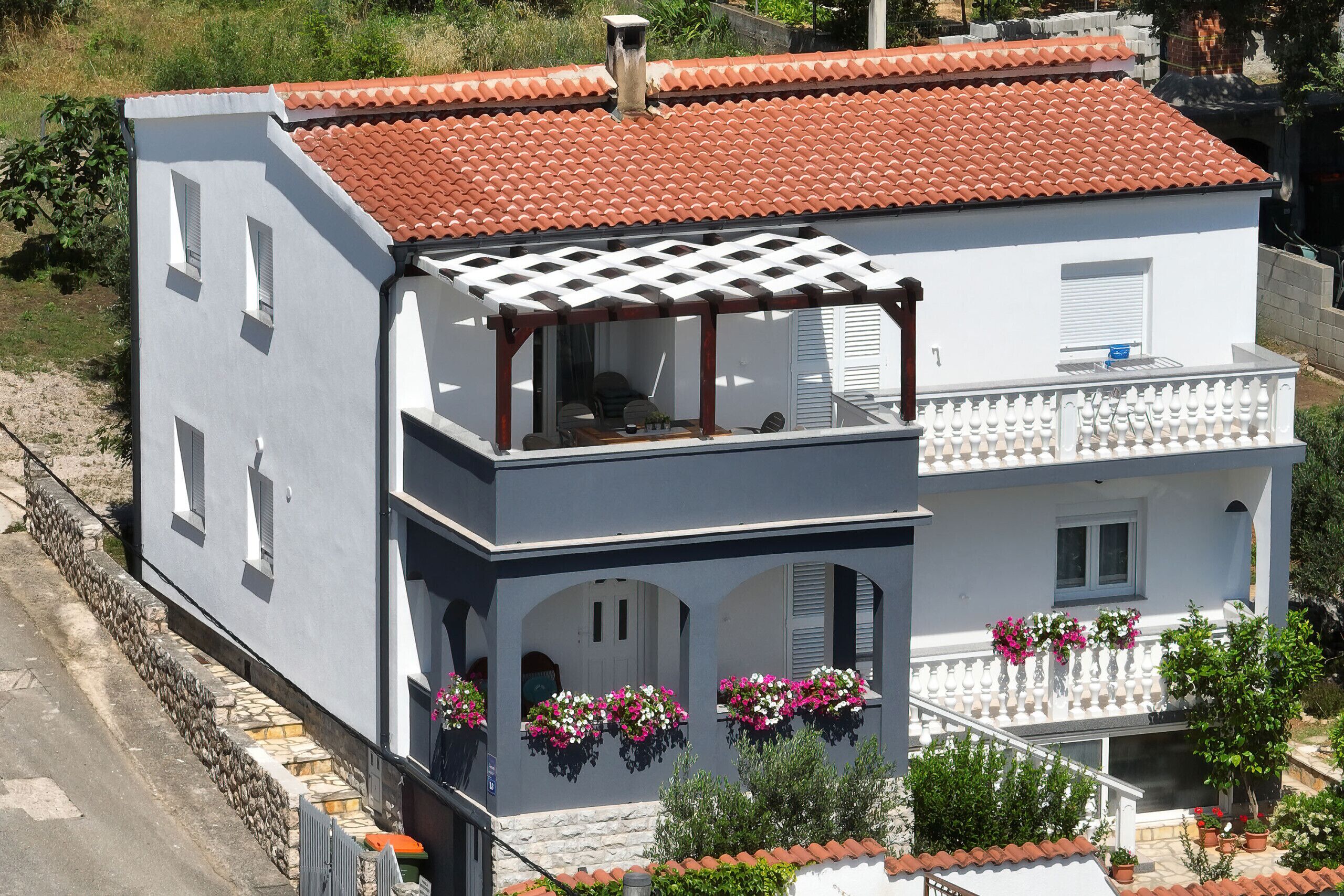 A two-story building with a red-tiled roof, a balcony with white railings, and flower boxes on the ground floor.