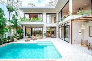 Et moderne, mereetages hus med swimmingpool, udendørs siddepladser og frodig vegetation.