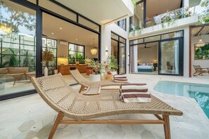 A modern interior with a pool area, lounge chairs, and a kitchen visible through large windows. - Feeels Villas 2 (Badung)