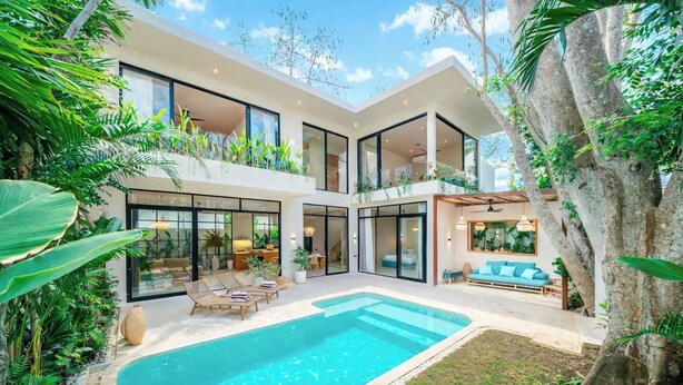Una casa moderna con piscina, amplios ventanales y exuberante vegetación.