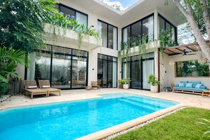 Et moderne hus med swimmingpool, store vinduer og udendørs siddepladser.