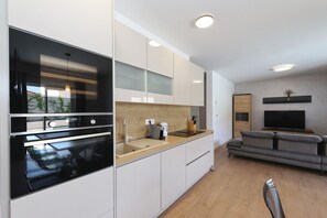 Eine moderne Küche mit eingebautem Ofen, Spüle und Arbeitsplatte. Im Wohnbereich befindet sich ein graues Sofa und ein Fernseher.