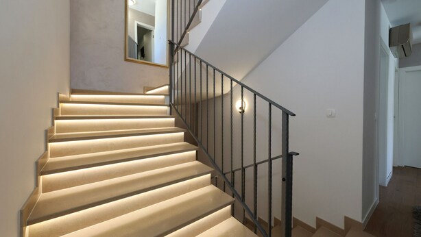 Una escalera con barandilla e iluminación, que conduce a un piso superior.