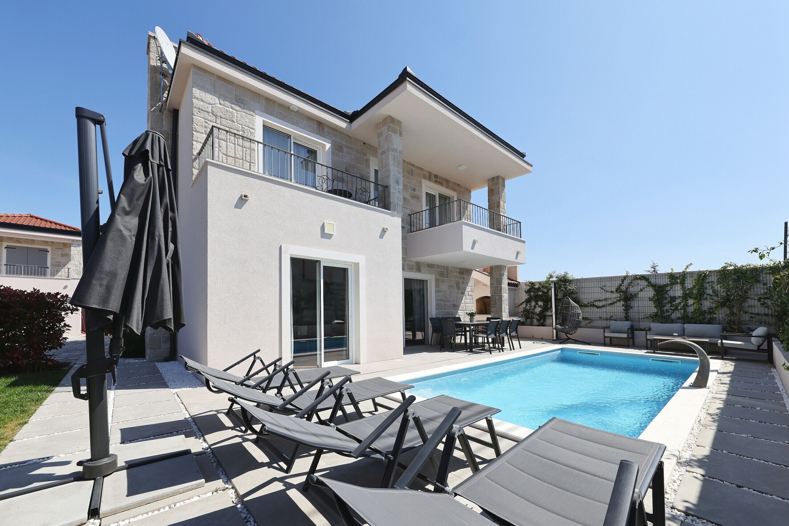 A two-story house with a swimming pool, outdoor seating, and a covered patio area.