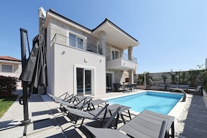 Ein zweistöckiges Haus mit Swimmingpool, Sitzgelegenheiten im Freien und einer überdachten Terrasse.