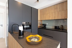 A modern kitchen with a built-in oven, a coffee maker, and a unique yellow bowl on the counter. - Apartment Hugo near the Sea (Privlaka)
