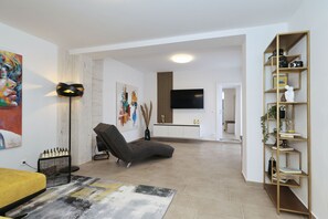 Ein modernes Wohnzimmer mit einer Couch, einem Flachbildfernseher, einem Bücherregal und Kunstwerken an den Wänden.