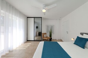 Ein modernes Schlafzimmer mit Bett, Deckenventilator, Stuhl und Blick durch eine Schiebetür.