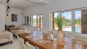 Een eetgedeelte met een lange houten tafel, meerdere stoelen en een vaas met bloemen.