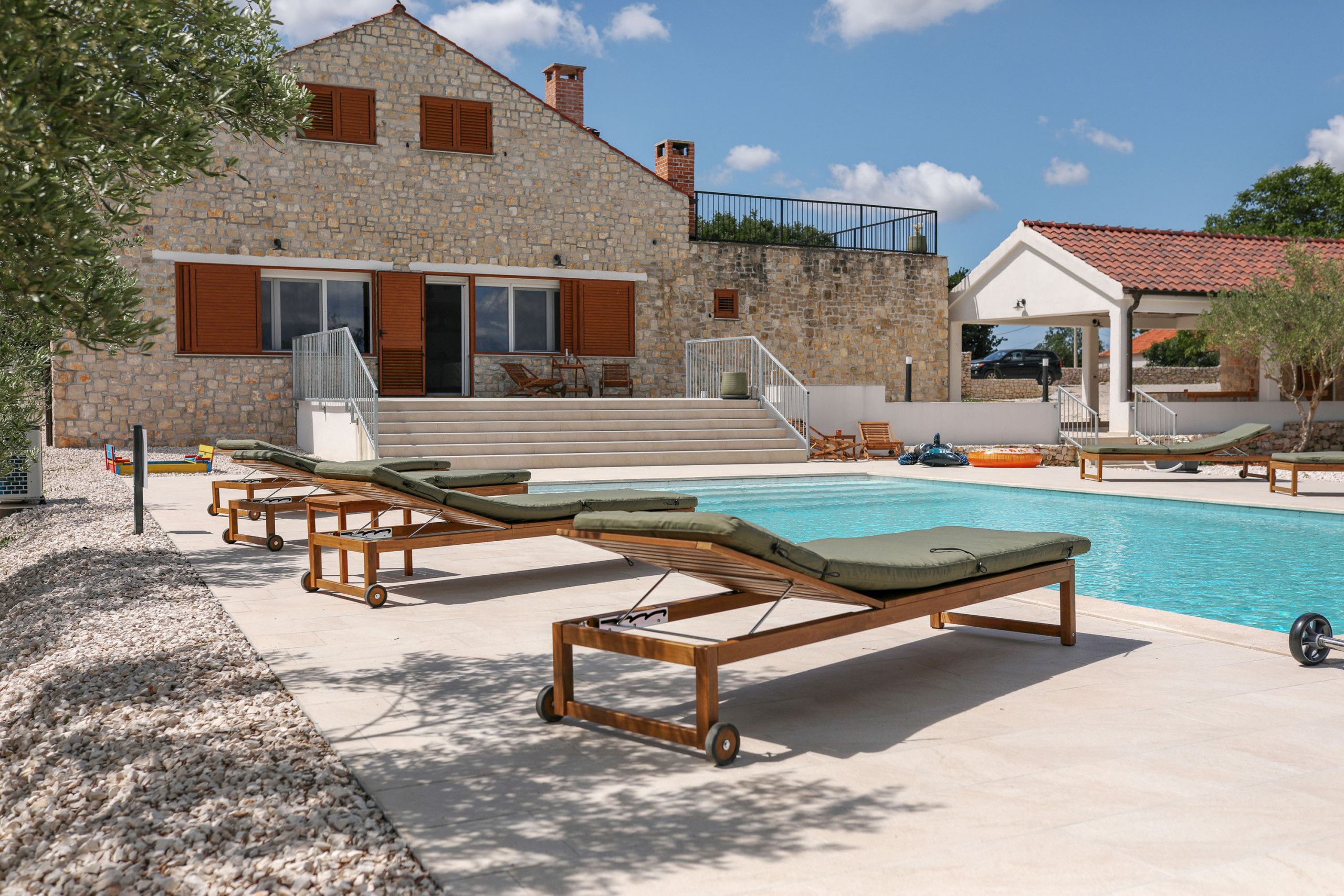 Ein Steinhaus mit Pool, Liegestühlen und überdachtem Bereich.