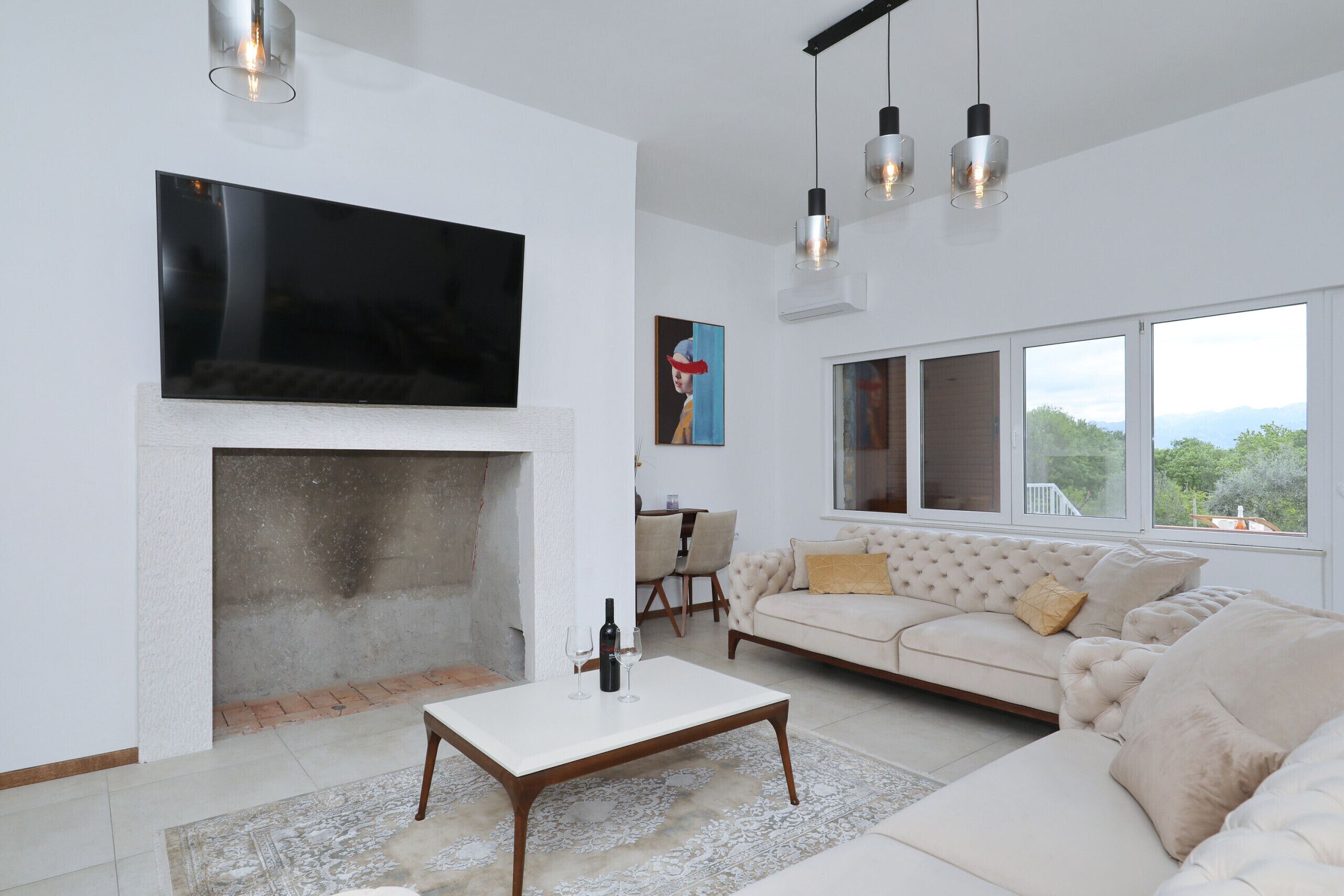 A living room with a flat-screen TV, a fireplace, a sofa, a coffee table, and pendant lights.