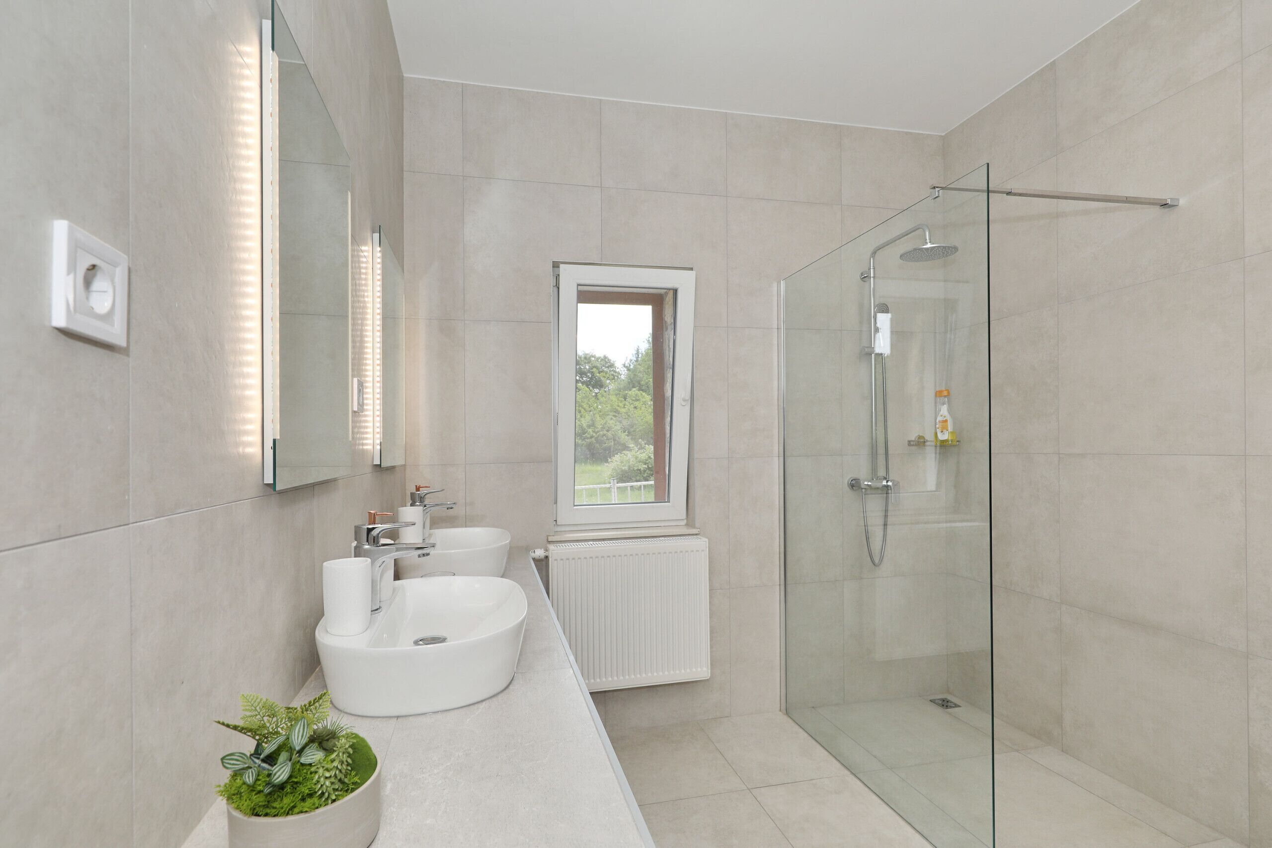 A modern bathroom with a glass shower enclosure, a white sink, and a window providing a view.