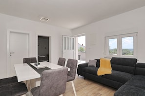 Ein modernes Wohnzimmer mit einem weißen Esstisch, grauen Stühlen, einem schwarzen Sofa und einer gelben Decke.