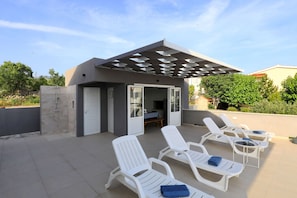 Eine Dachterrasse mit Sitzgelegenheiten, einer Pergola und einem kleinen Gebäude mit Tür und Fenstern.
