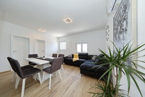 Ein moderner Wohnbereich mit Esstisch, Stühlen, einer Couch und einer großen Pflanze.