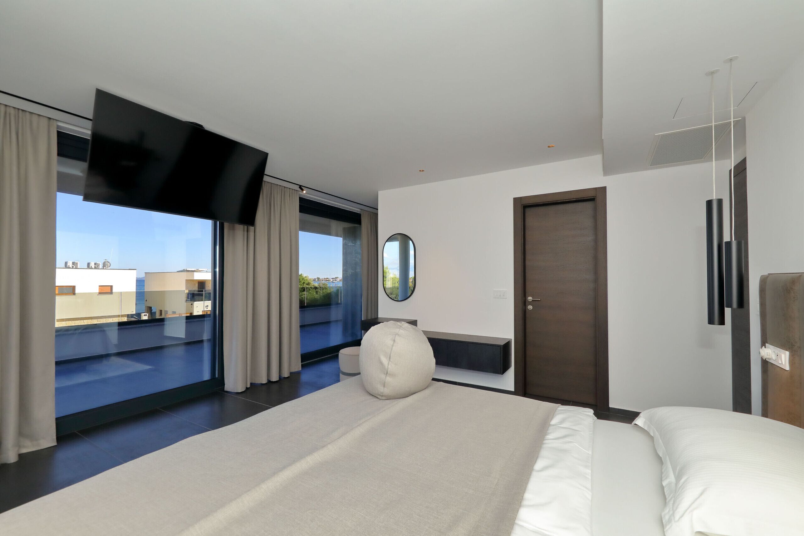 Een moderne hotelkamer met een groot bed, een flatscreen televisie, een ronde spiegel en uitzicht op de stad.