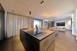 A modern kitchen with an island, a dining area with a sofa, and a large window with curtains. - Villa Suva Punta Luxe with Private Pool (Vir)