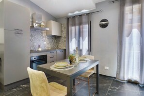 Una cuina moderna amb taula i seients per a dues persones, un rellotge a la paret i una finestra amb cortines.