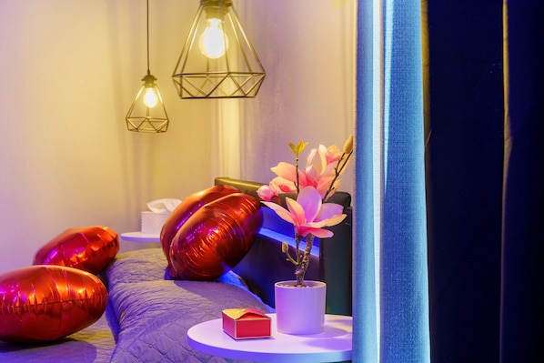 Un dormitorio con cama, almohadas, una mesita de noche con un florero y lámparas colgantes.
