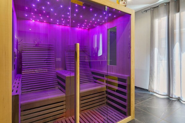 Una sauna amb seients de fusta, un envàs de vidre, il·luminació morada i un sòl de rajola.
