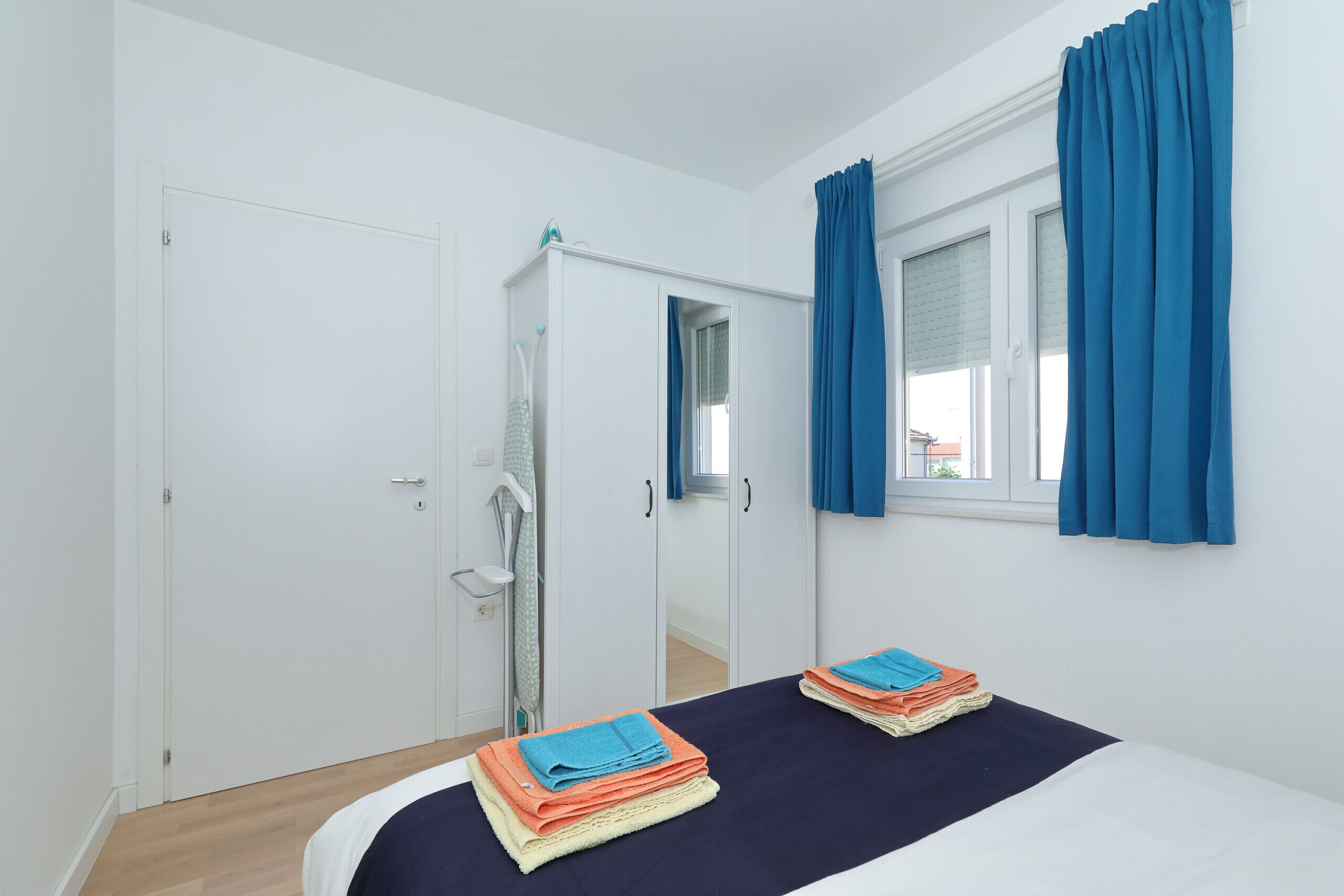 A bedroom with a bed, a wardrobe, a window with curtains, and a door.