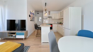 En modern lägenhet med TV, matplats, kök och en liten köksö.